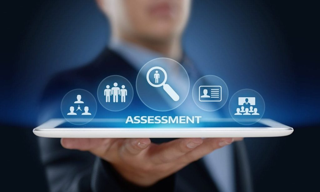 A person holding a tablet displaying digital icons related to assessment, including people, a magnifying glass, and ID graphics, symbolizing evaluation and performance review tools.